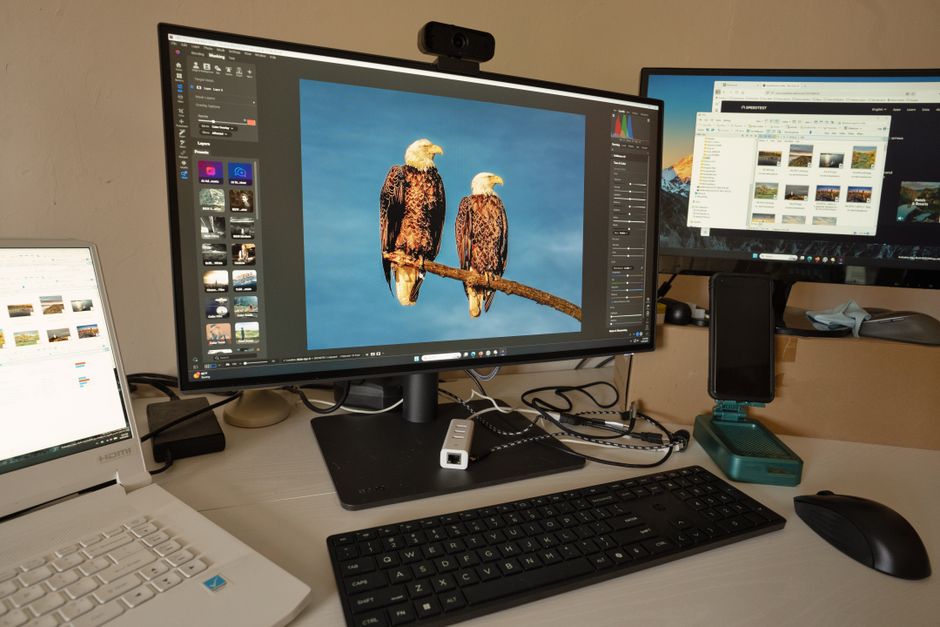 A desk setup showing photo editing software on multiple monitors, a keyboard, and peripherals.