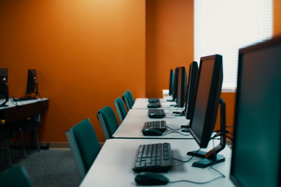 Modern computers with keyboards and mice placed in row on table with chairs in contemporary workplace with orange walls